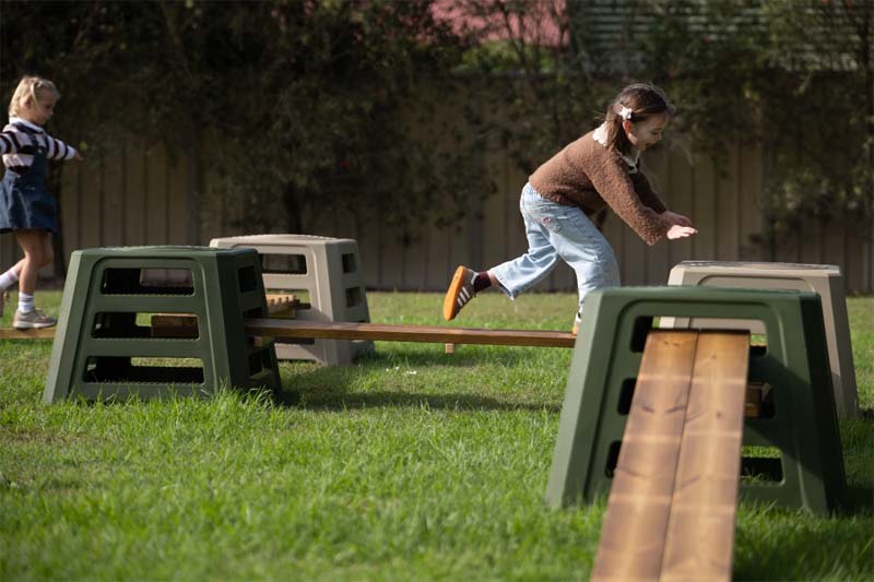 A child running and leaping along the Classic Outdoor timber balance trail between steppers