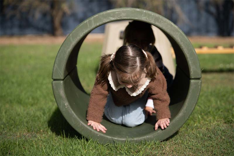 A child crawling through the Classic Outdoor discovery tunnel in a garden