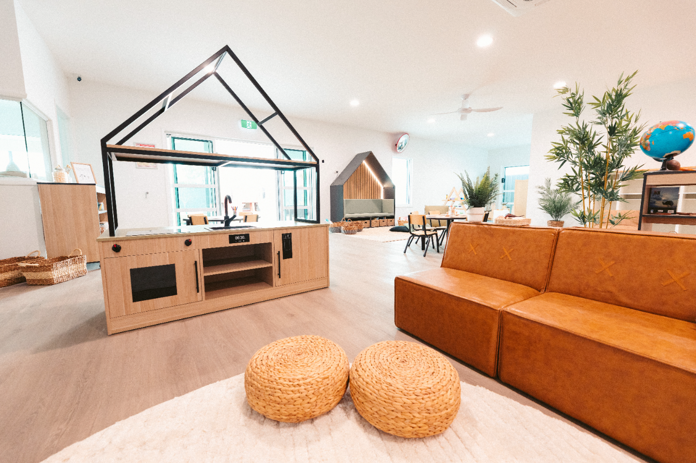 House-frame play kitchen beside a tan modular lounge and woven ottomans