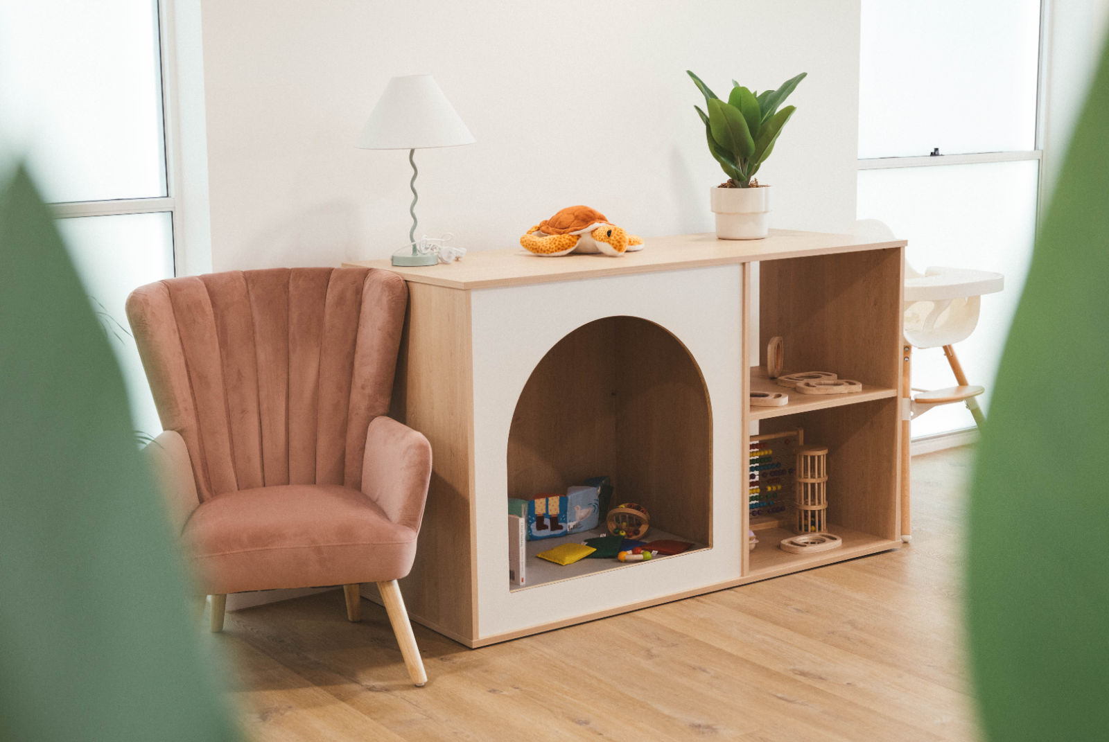Blush velvet armchair beside a timber arch cubby unit with toys and a plant