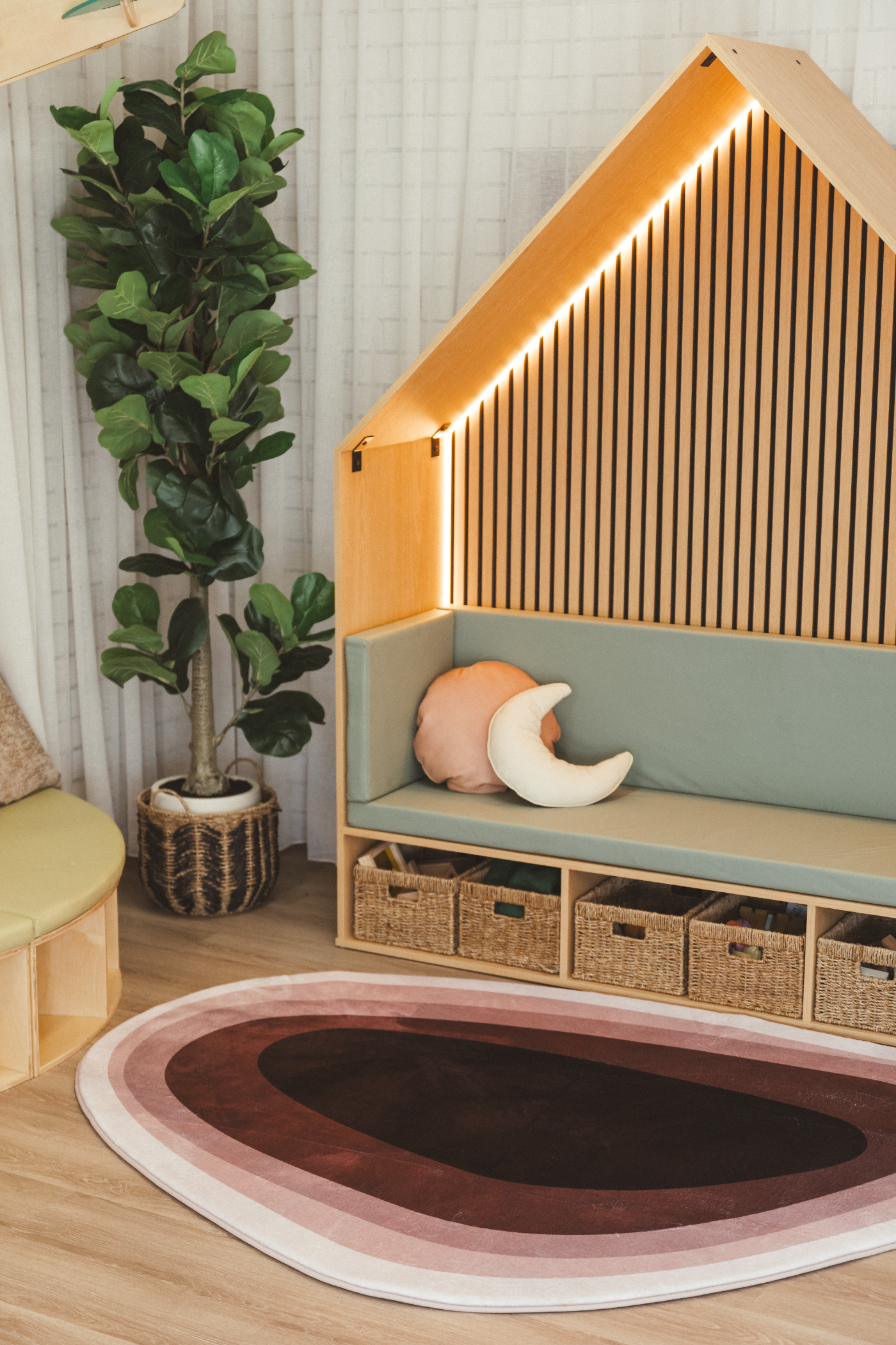 A timber house-frame reading nook with sage cushions, woven baskets, a plant and a layered rose rug